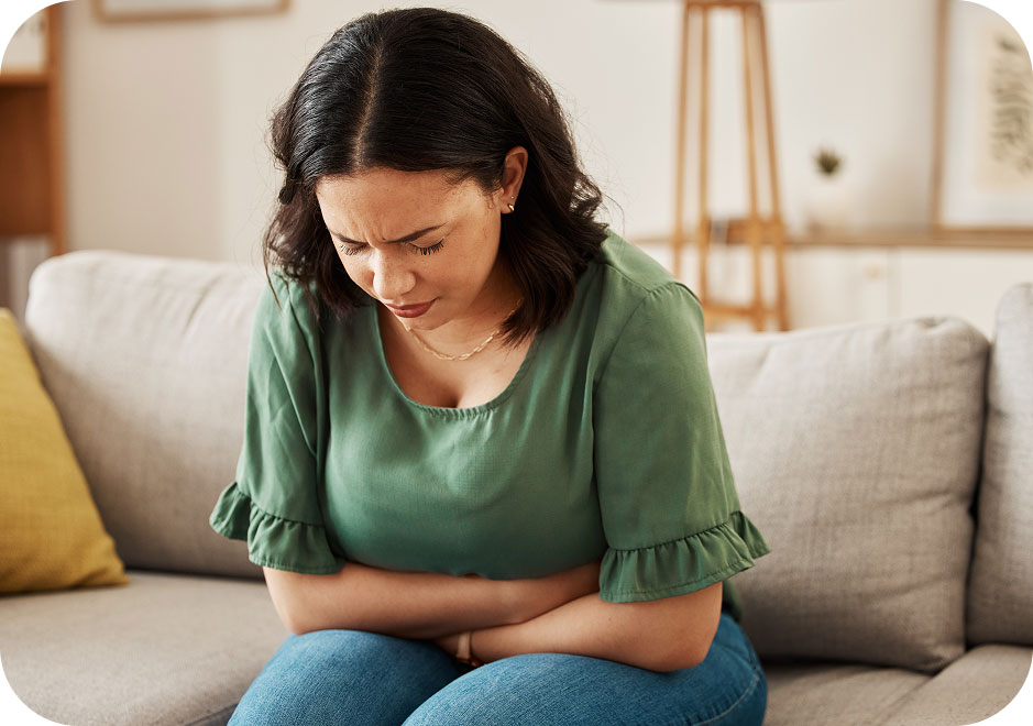 Woman on sofa at home, experiencing stomach pain and stress.