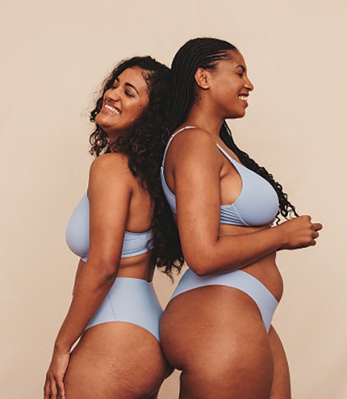 Two happy young women in blue underwear embracing their natural bodies and curves against a studio background.