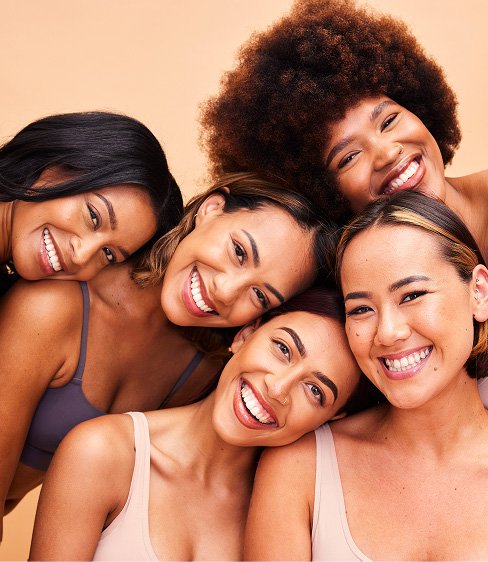 Portrait of diverse women with makeup, smiling and embracing beauty, skincare, and self-care against a brown studio background.